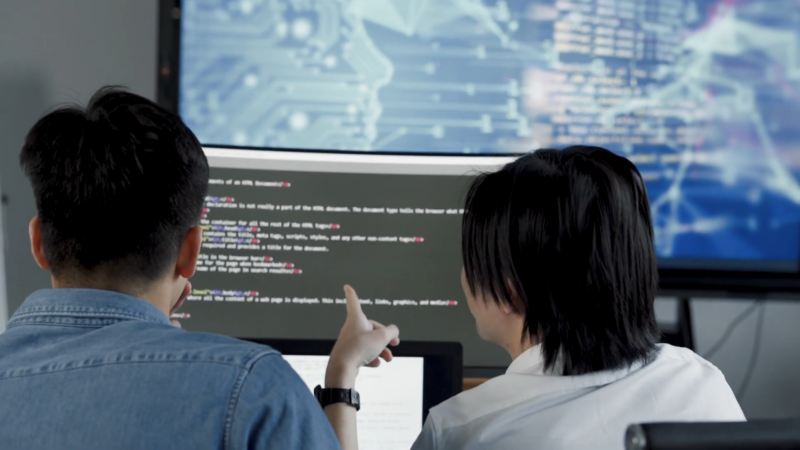 Two People Analyzing Code on A Computer Screen, Discussing Technical Details