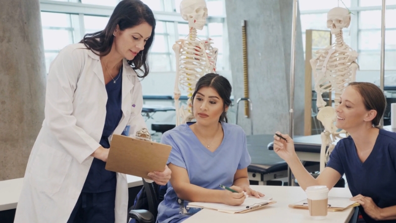 A healthcare professional in a lab coat discusses with two students in scrubs