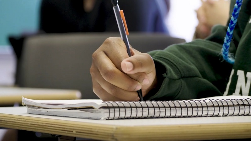 Close-up of a student's hand writing in a spiral notebook during class, focusing on academic engagement