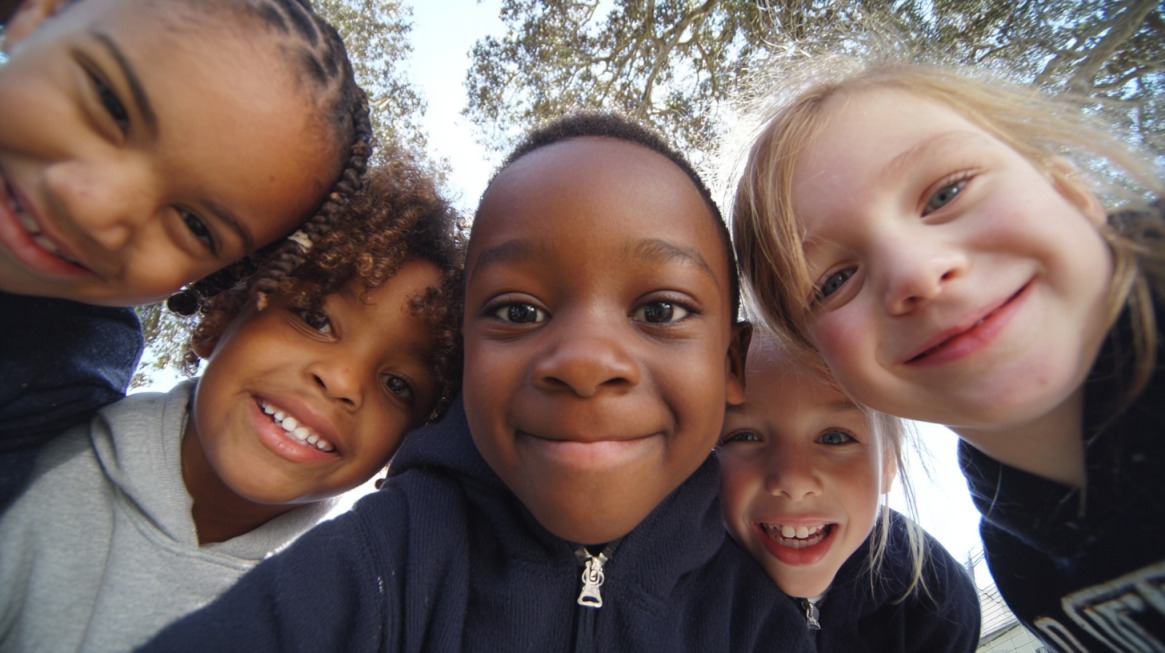A group of young children smiling and looking into the camera outdoors