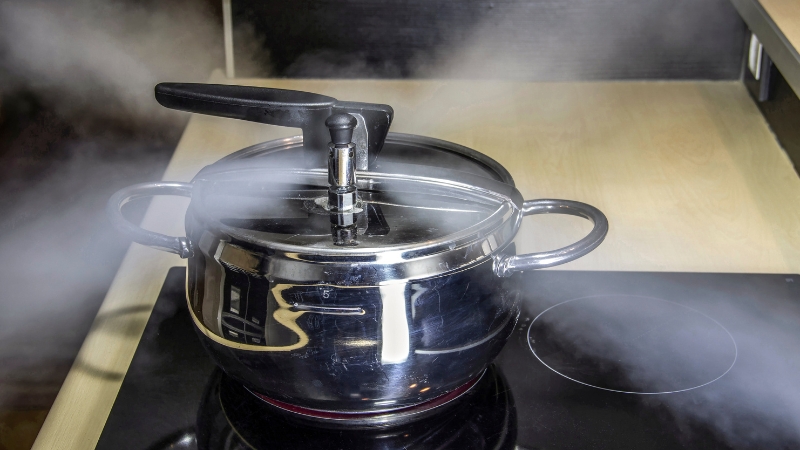 Steam escapes from a pressure cooker on a stove, showing physics principles of heat and temperature