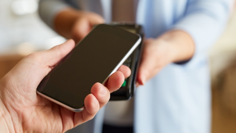 Phone held to payment terminal showing physics principles in NFC Pay