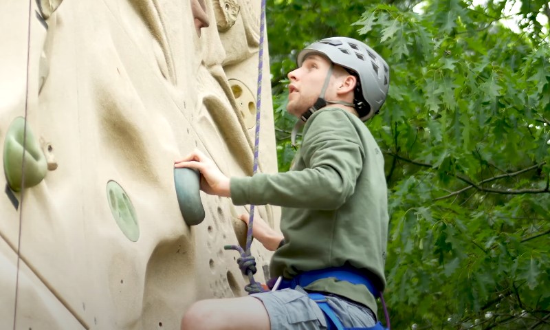 A kid scaling a natural rock wall in an outdoor setting