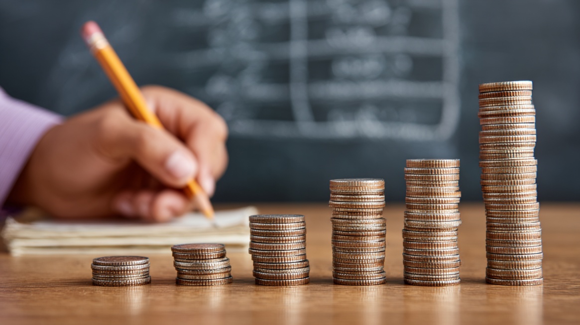 Stacks of coins increasing in height with a person writing in the background