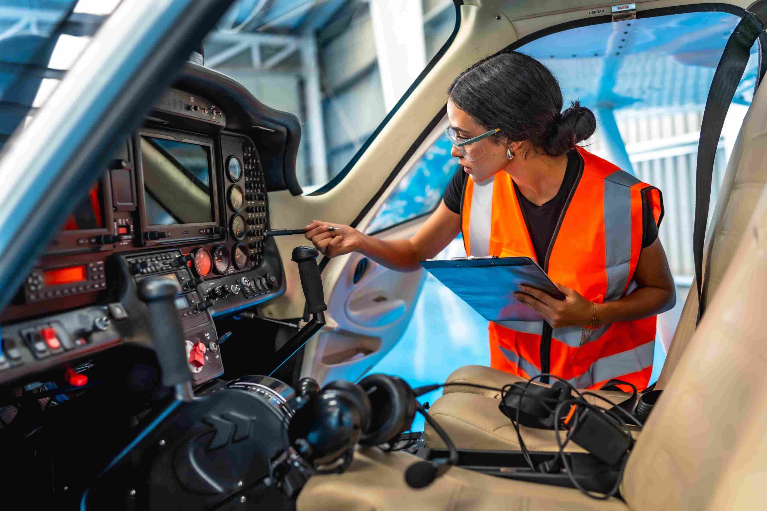 Technician inspecting aircraft cockpit controls and avionics equipment while holding a checklist.