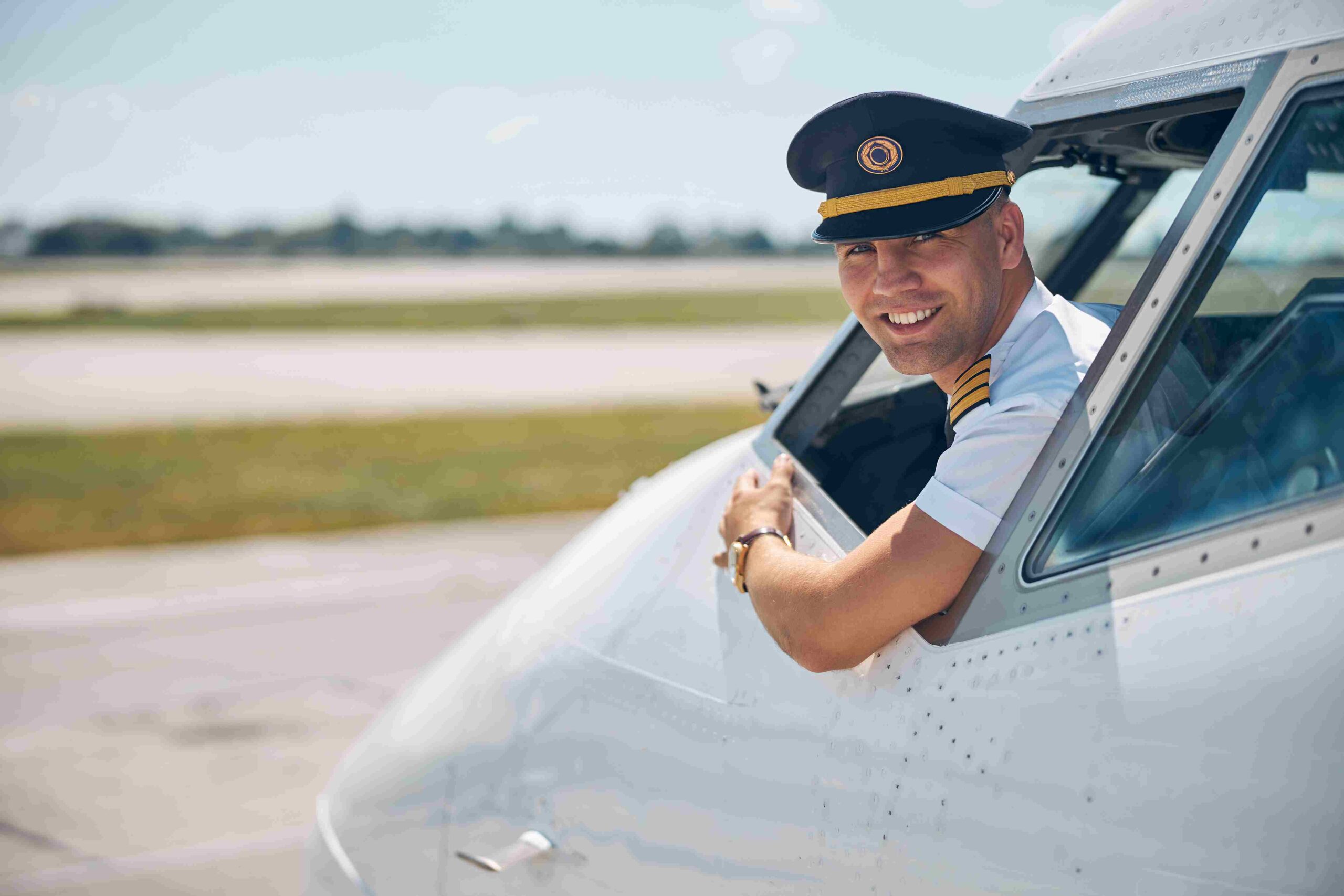 Commercial pilot smiling from the cockpit window of an airplane on the runway.