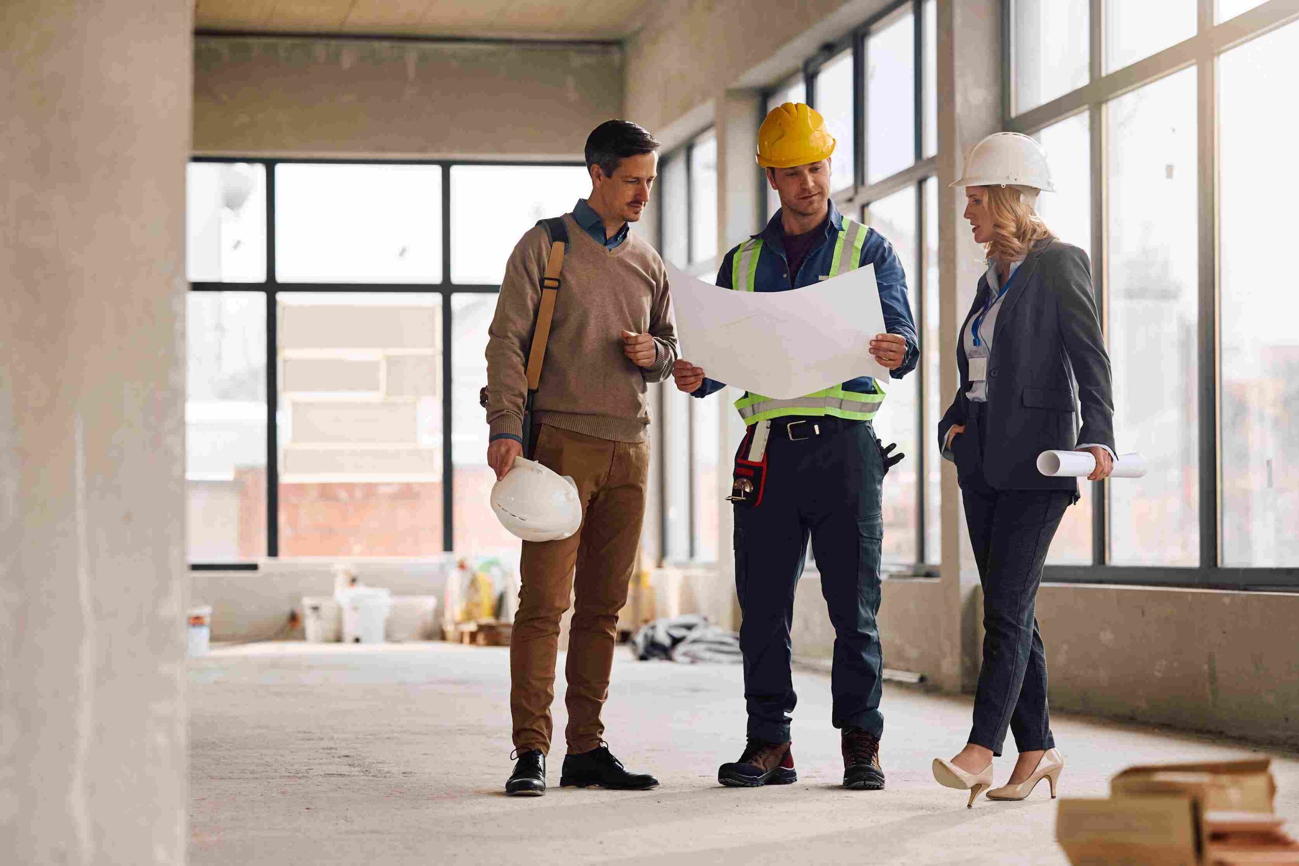 Construction professionals reviewing building plans inside a construction site while wearing safety helmets