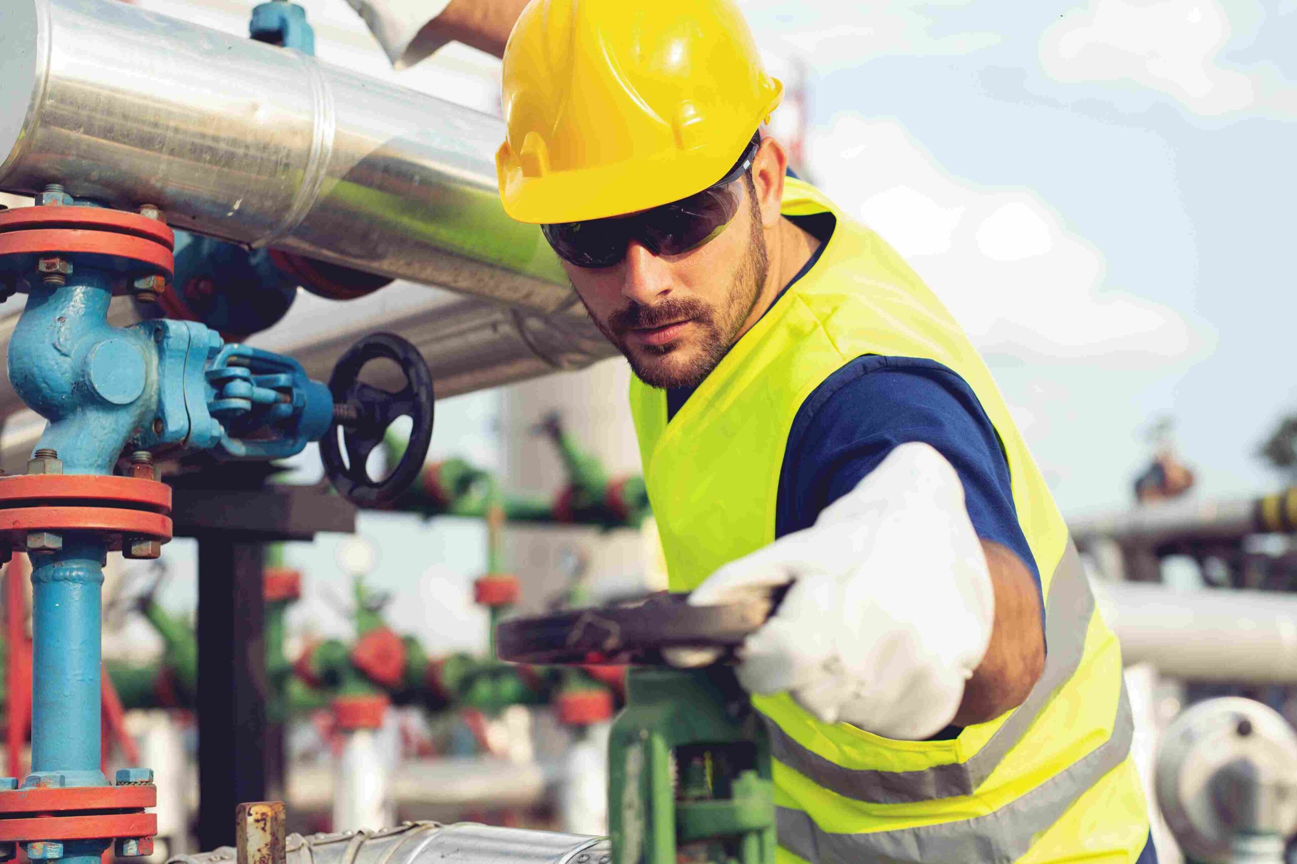Industrial worker wearing safety gear while operating machinery at a refinery facility